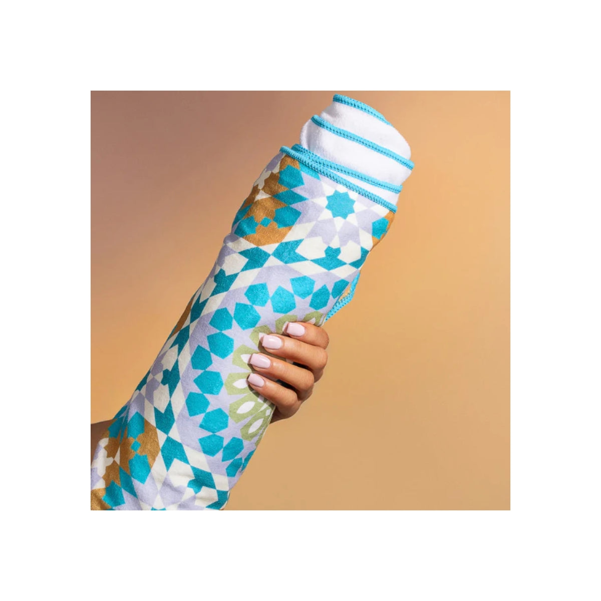 Hånd holder farverigt Bounce Curl Micro-fiber Towel med blå og grønne mønstre mod beige baggrund.
