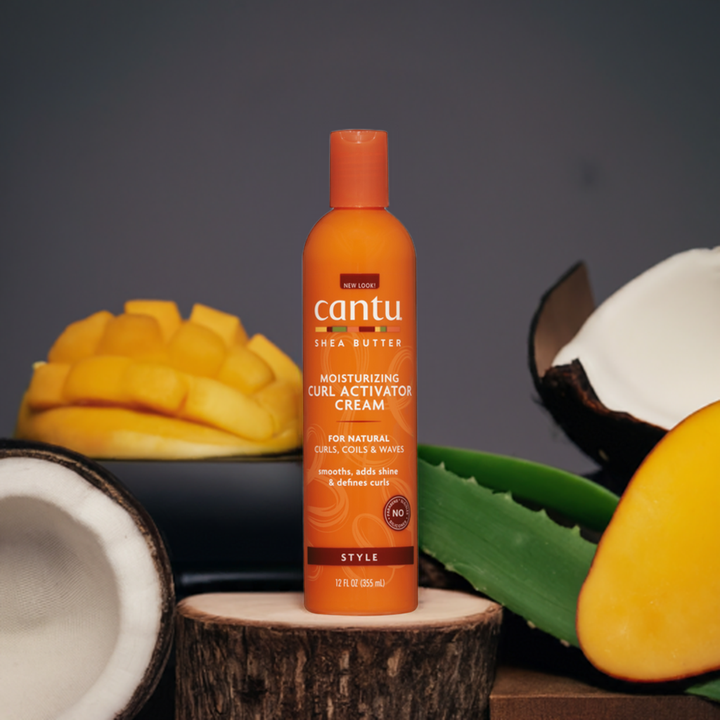 Nærbillede af en orange flaske Cantu Shea Butter Curl Activator. Flasken står foran tropiske frugter, der symboliserer produktets naturlige ingredienser.