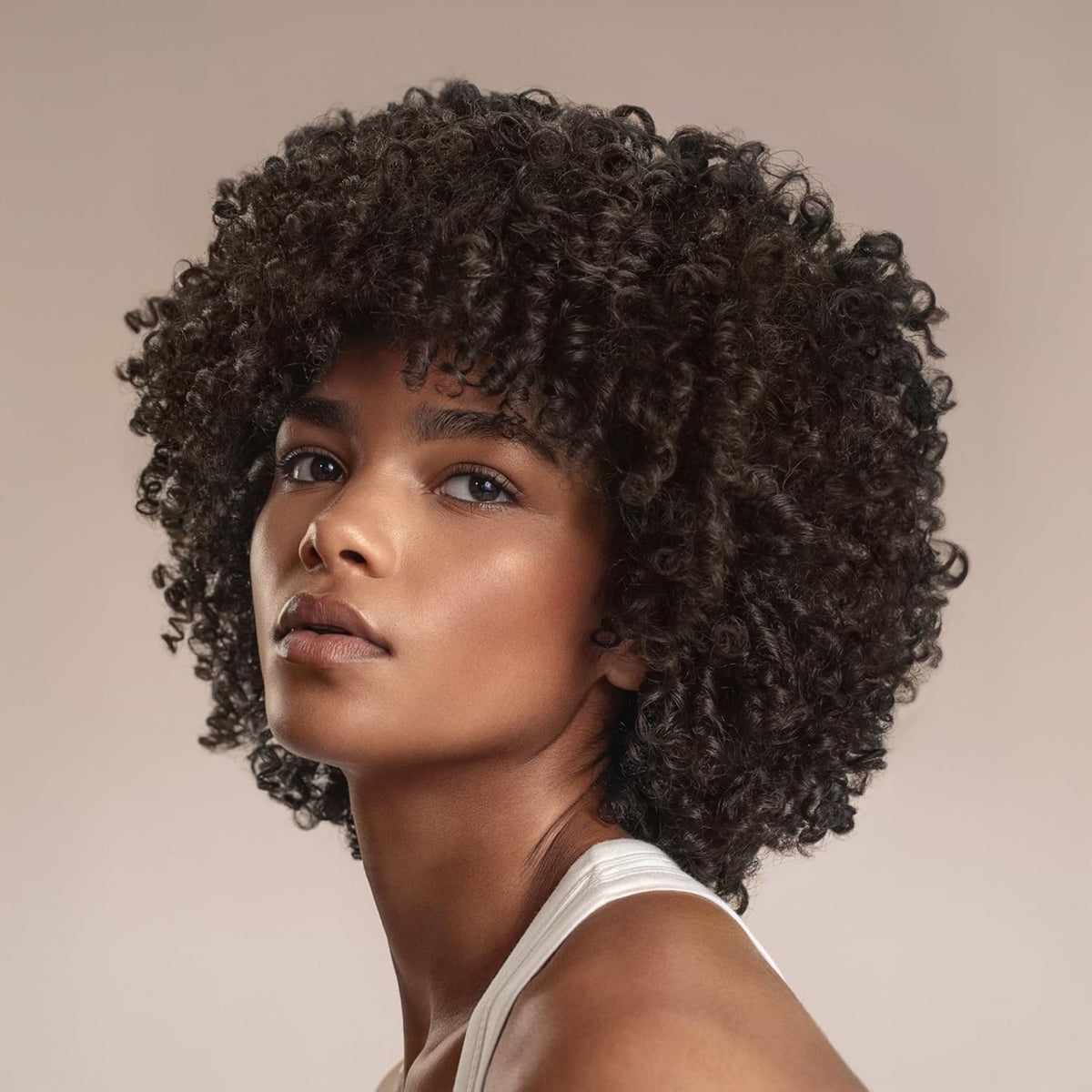 Kvinde med naturligt krøllet afro-hår i mørkebrun nuance og curtain bangs, iført hvid linned.