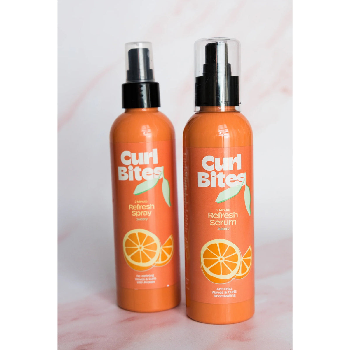 To orange Curl Bites-flasker: 2 Minute Refresh Spray og Refresh Serum med appelsinmotiv på lyserød baggrund.
