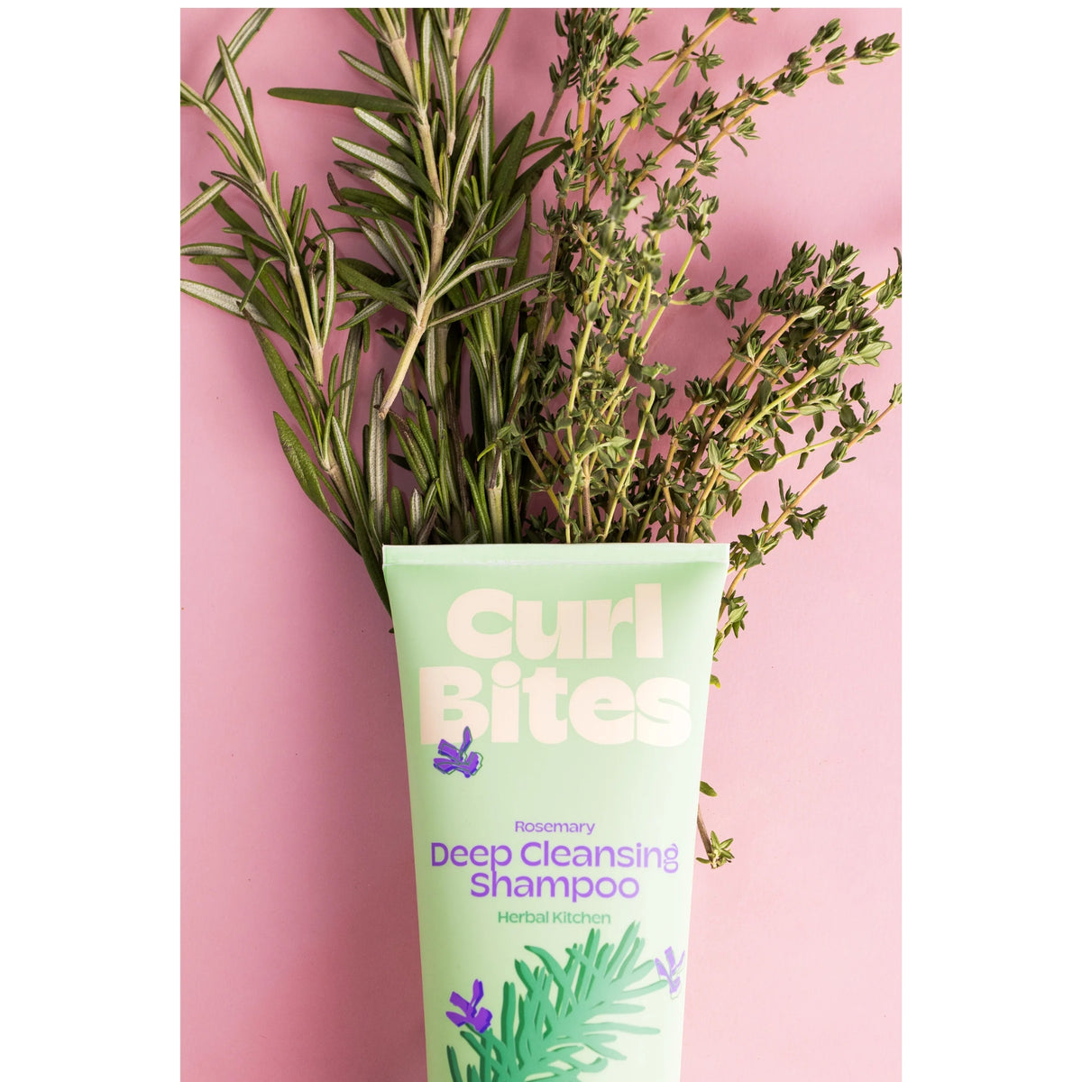 Curl Bites Rosemary Deep Cleansing Shampoo tube omgivet af friske rosmarin- og timiankviste på lyserød baggrund.
