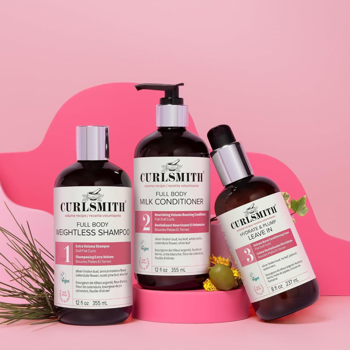 Curlsmith Full Body volumen-serie: shampoo, mælkebalsam og leave-in på lyserød baggrund med grønne blade.