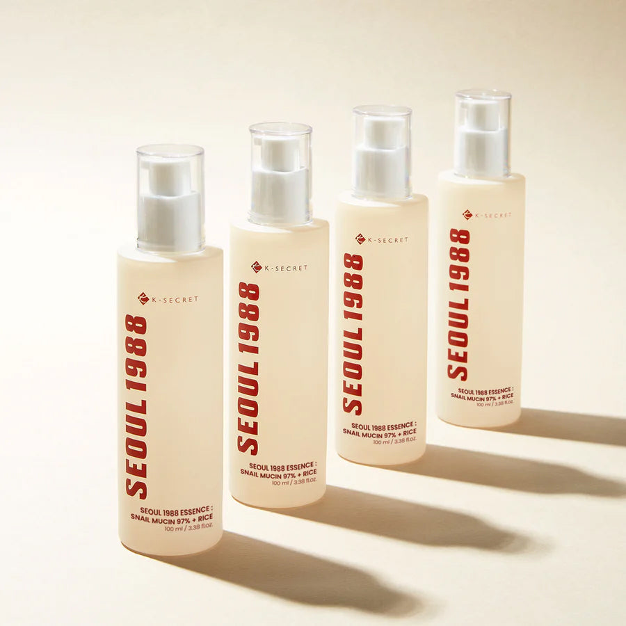 Fire flasker K-Secret Essence: Snail Mucin 97% + Rice 100 ml står på lyst underlag med rød tekst og minimalistisk design.