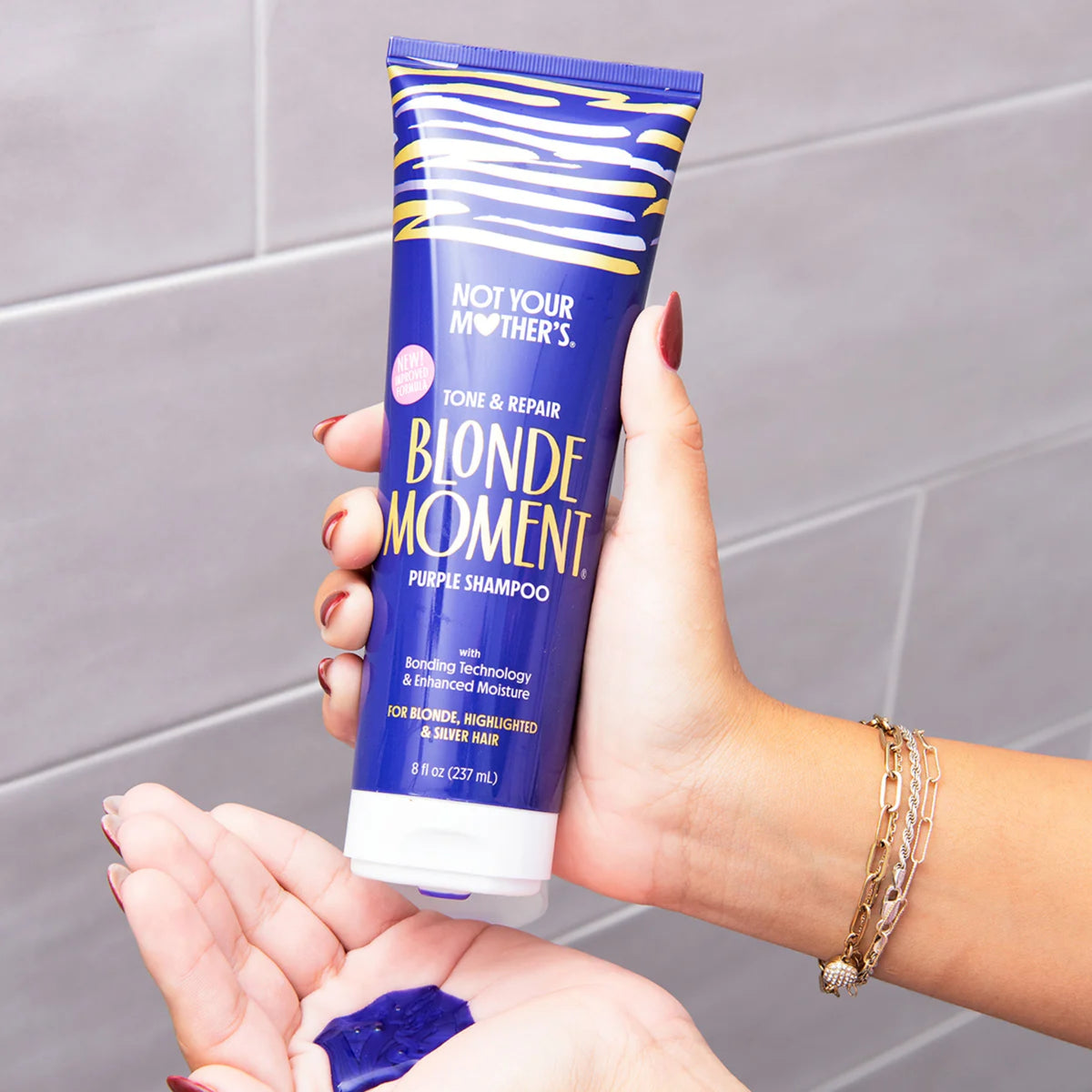 Not Your Mother's Blonde Moment purple lilla shampoo holdes i hånden med lilla produkt i håndfladen.