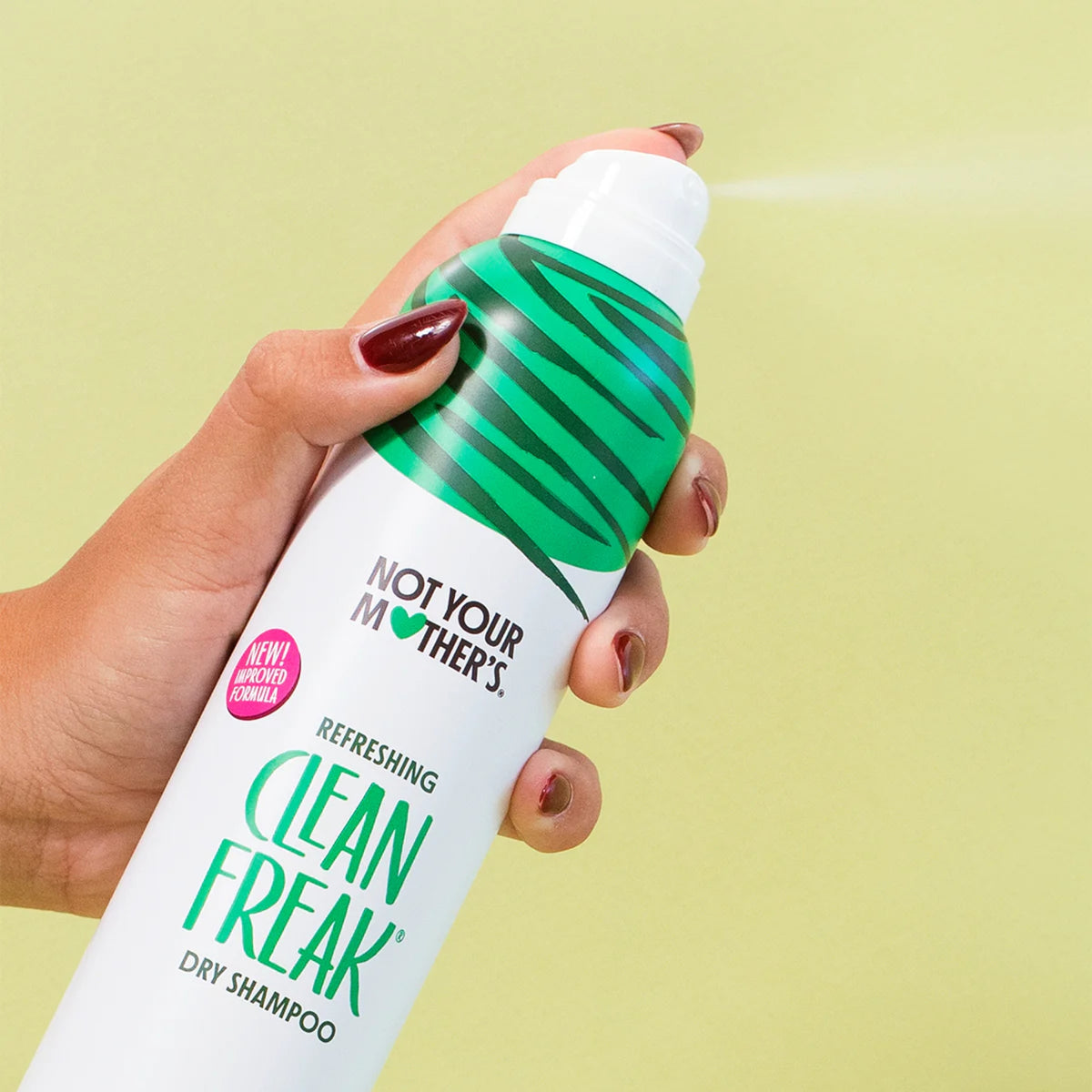 Hånd sprayer Not Your Mother's Clean Freak dry shampoo mod grøn baggrund.