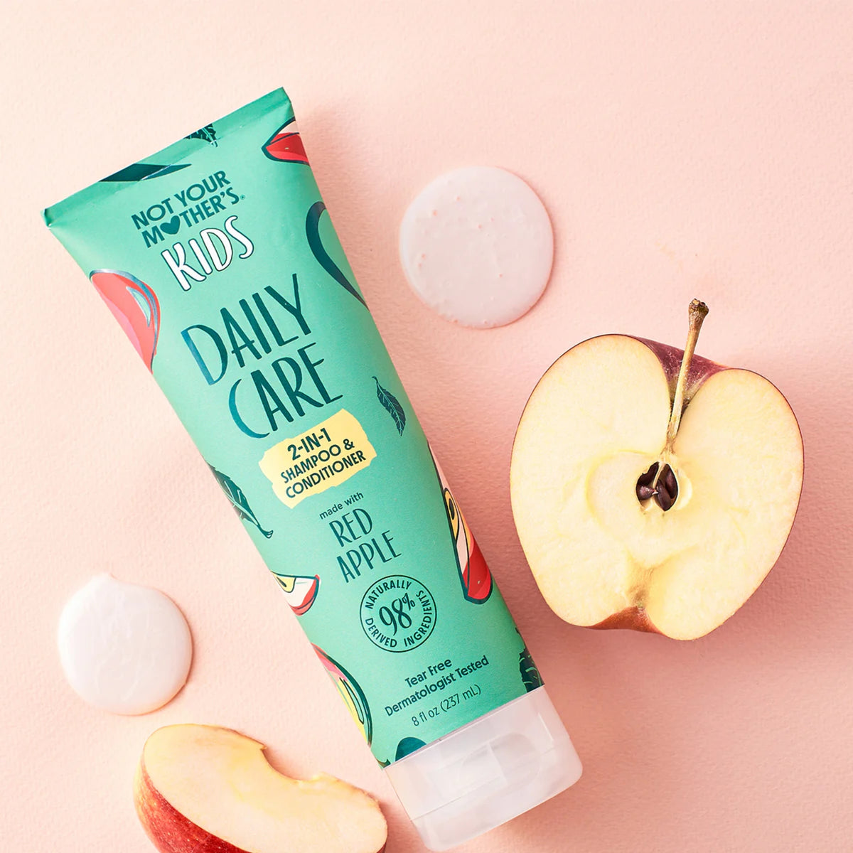 Not Your Mother's Kids Daily Care 2-i-1 shampoo og balsam med rødt æble ved siden af friske æbleskiver.