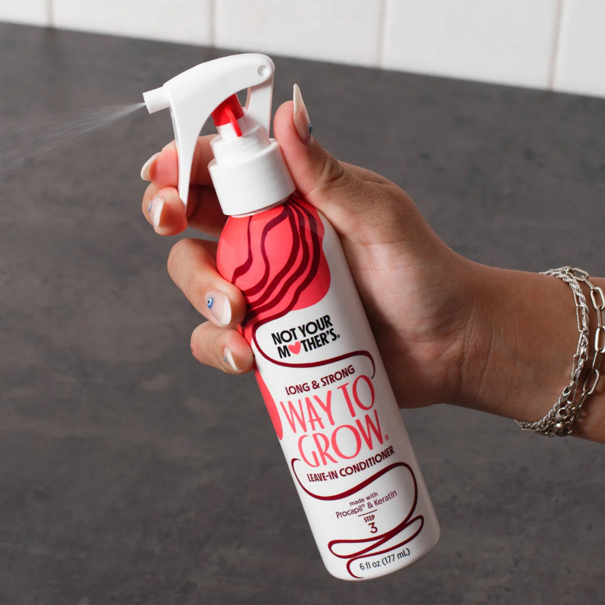 Hånd sprayer Not Your Mother's Way To Grow leave-in conditioner fra hvid og rød flaske.