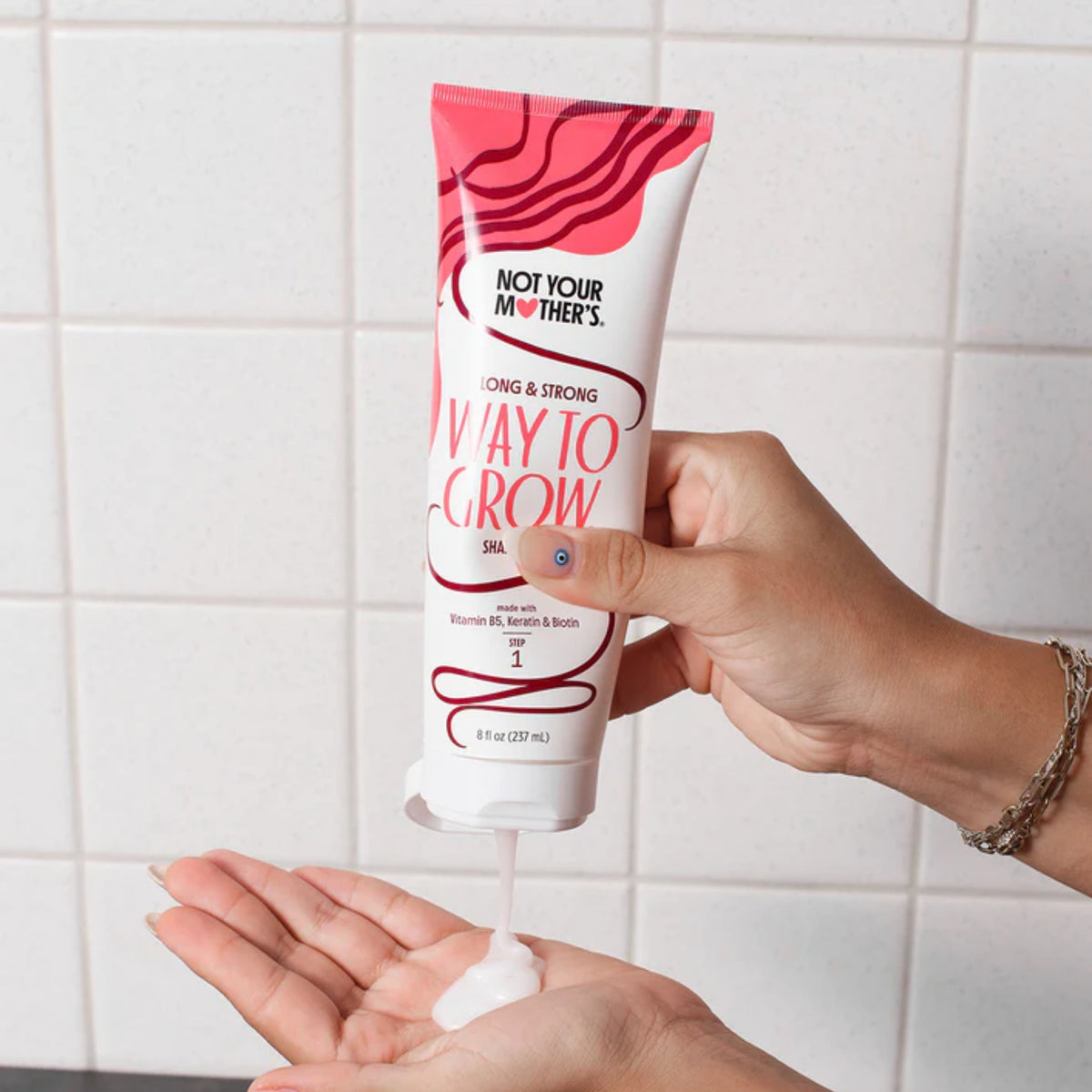 Not Your Mother's Way to Grow shampoo presses ud i hånden foran hvide fliser i badet.