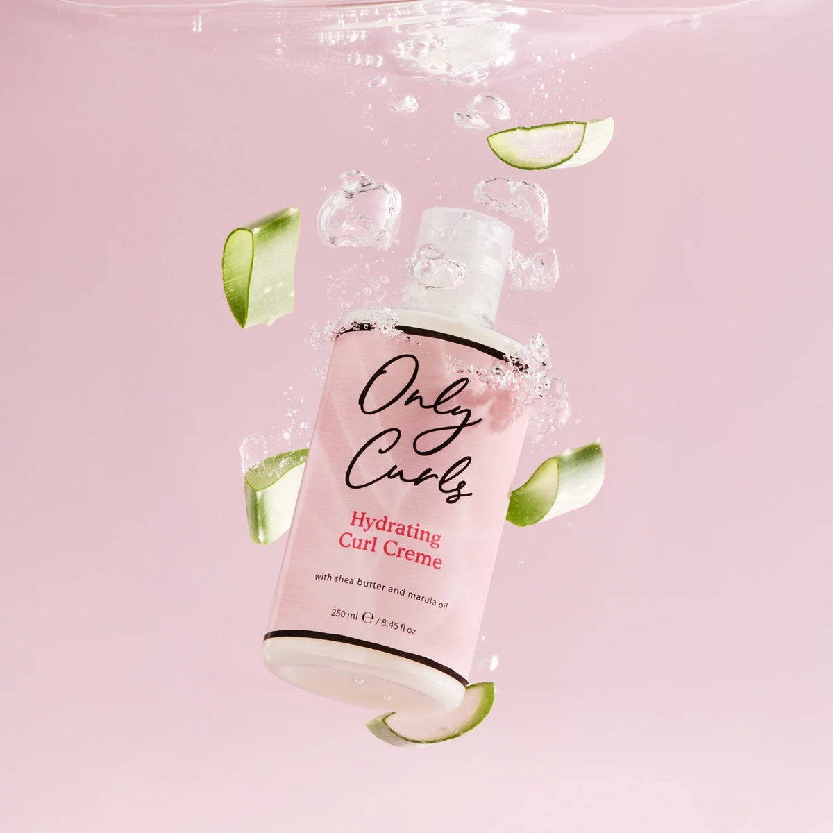 Only Curls Hydrating Curl Creme-flaske nedsænket i vand med agurkeskiver og bobler på lyserosa baggrund.