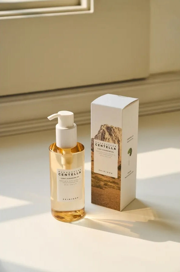 Flaske SKIN1004 Madagascar Centella Light Cleansing Oil 200ml ved siden af æstetisk emballage i sollys på vindueskarm.