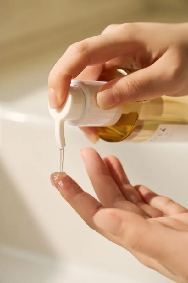 Hånd doserer SKIN1004 Madagascar Centella Light Cleansing Oil 200ml med pumpe over vask i blødt, varmt lys.