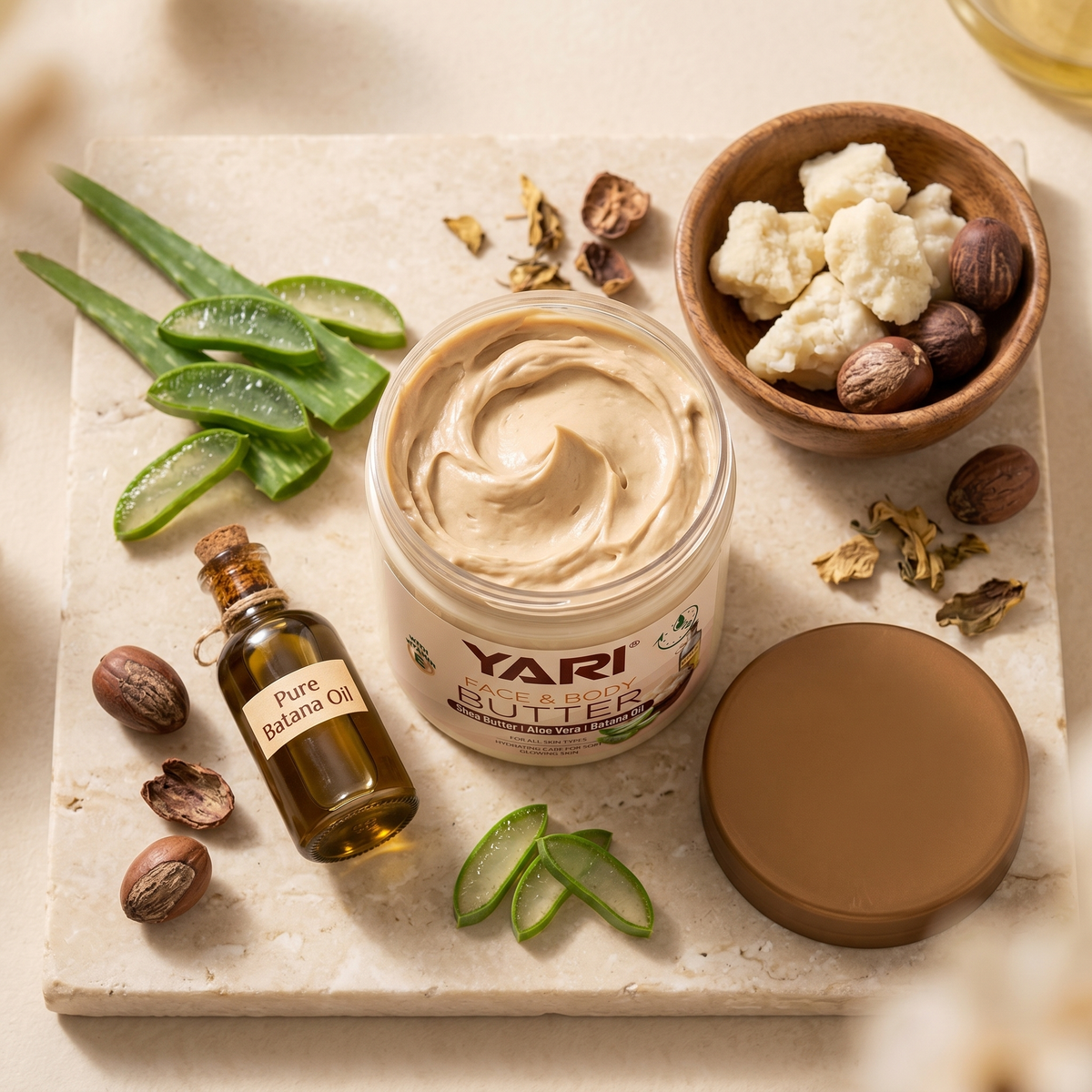 Yari Face & Body Butter med shea butter, aloe vera og batana olie omgivet af naturlige ingredienser på stenplade.
